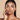 Woman in mid 20's touching her face against a beige background